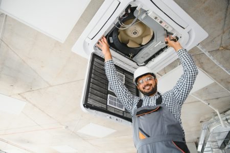 Concentrated young Indian engineer setting up air conditioner.